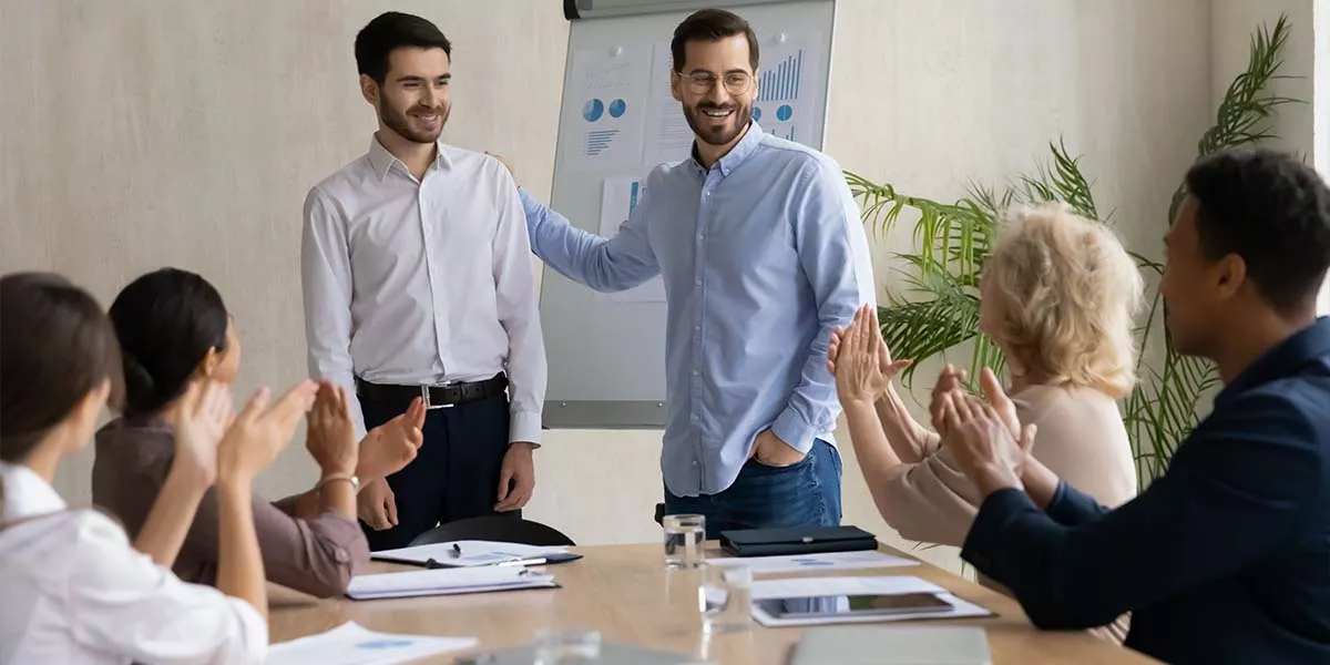 Glücklicher junger Geschäftsmann stellt dem Team einen neuen männlichen Angestellten vor.