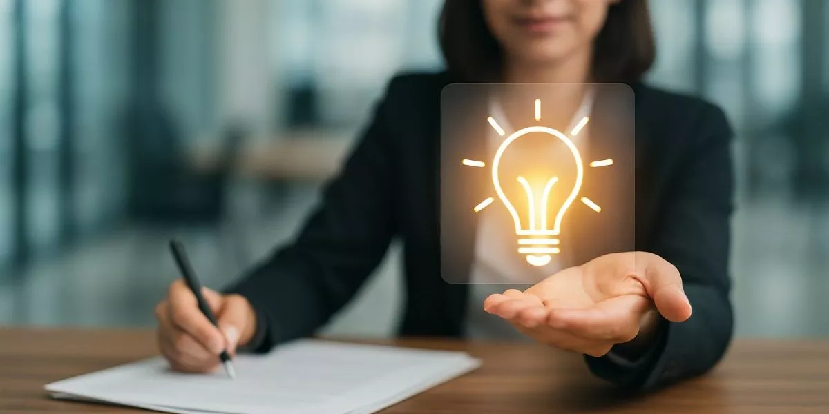 Innovationsmanagerin sitzt am Schreibtisch und hält ein Glühbirnensymbol in der Hand