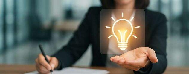 Innovationsmanagerin sitzt am Schreibtisch und hält ein Glühbirnensymbol in der Hand