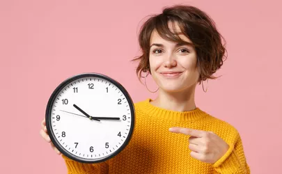 Frau zeigt auf eine große Uhr in ihrer Hand