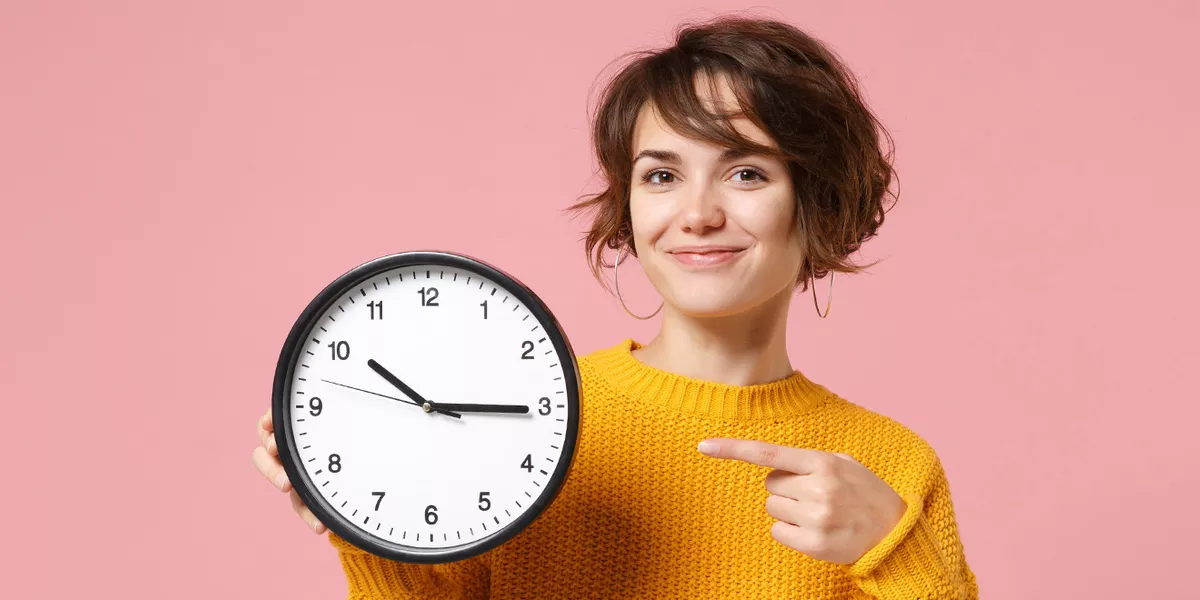 Frau zeigt auf eine große Uhr in ihrer Hand