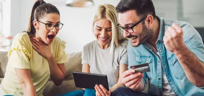 Zwei Frauen und ein Mann im Wohnzimmer mit Kreditkarte und digitalem Tablet