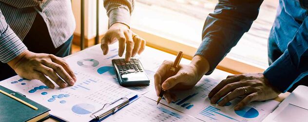 An einem Schreibtisch mit vielen Plänen, Schaubildern und Statistiken arbeiten zwei Leute