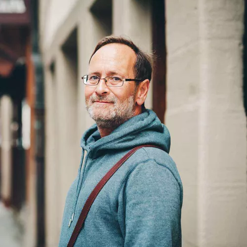 Mann in blauer Jacke mit braunen Haaren, Brille und grauem Bart