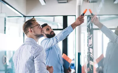 Mann zeigt seinem Kollege an einem Flip-Chart die Ziele seines Projekts