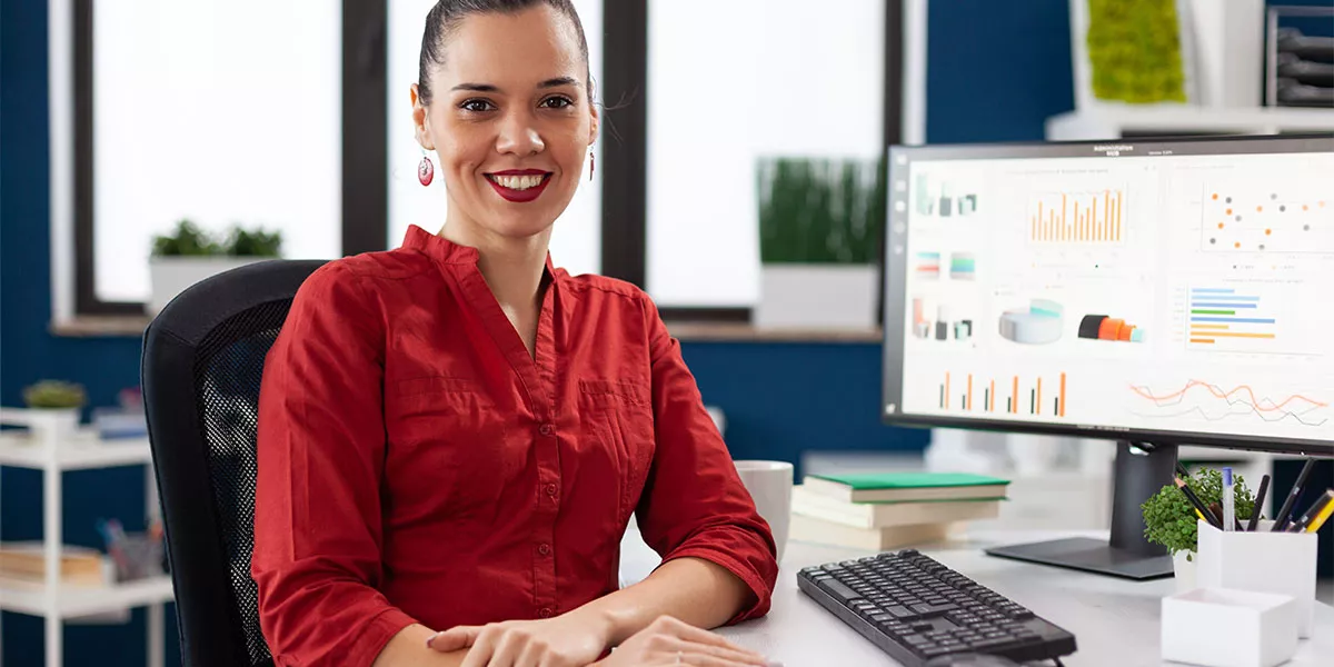 eine Frau in rotem Hemd sitzt am Schreibtisch mit Desktop-Computer