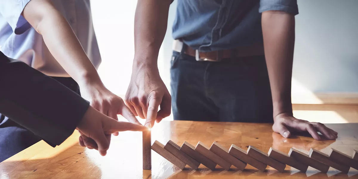 Business-Team stützt einen Holzklotz am Ende einer Dominoreihe und bewahrt ihn vor dem Umfallen