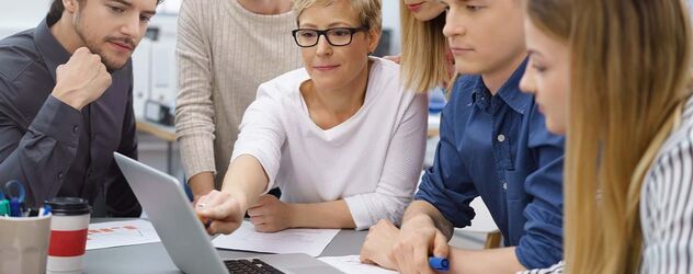 Geschäftsfrau erklärt jungen Kollegen etwas am PC