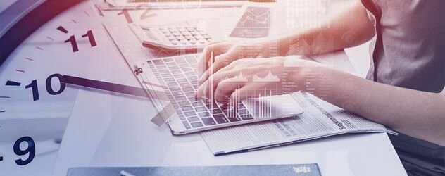 Nahaufnahme einer Hand, die auf einem Laptop Tastatur tippt und im Hintergrund eine Uhr