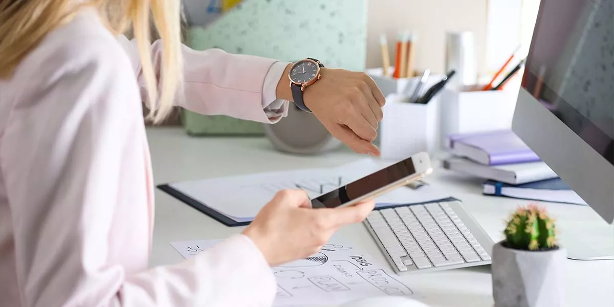 Junge Frau überprüft die Zeit auf ihrer Armbanduhr am Arbeitsplatz