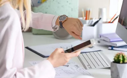 Junge Frau überprüft die Zeit auf ihrer Armbanduhr am Arbeitsplatz