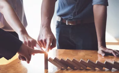 Business-Team stützt einen Holzklotz am Ende einer Dominoreihe und bewahrt ihn vor dem Umfallen